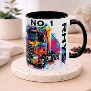 May include: A white ceramic mug with a black interior and handle. The mug features a colorful illustration of a semi-truck with the text "NO. 1" and the name "RHYS". The truck design incorporates a vibrant mix of colors.