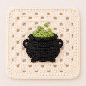 Op de afbeelding: Een vierkante gebroken witte gehaakte onderzetter in granny square-stijl met een centraal geplaatste zwarte gehaakte ketel gevuld met textuurrijke lichtgroene bubbels. De ketel heeft twee kleine handvatten aan de zijkanten en drie korte pootjes.