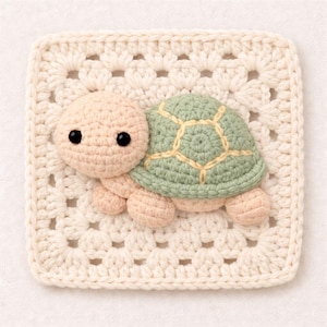 Op de afbeelding: Een gehaakte schildpad applicatie in pastelkleuren. De schildpad heeft een beige kop en ledematen, een groene schild met gele details en zwarte ogen. Het is bevestigd aan een crèmekleurig vierkant, wat een charmant, handgemaakt ontwerp creëert.