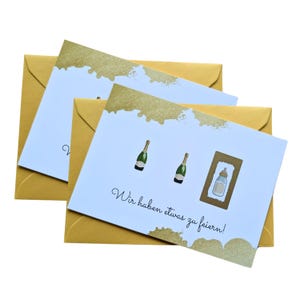 May include: Greeting cards with gold accents and matching envelopes. The cards feature illustrations of champagne bottles and a baby bottle, with the text "Wir haben etwas zu feiern!" in a script font.