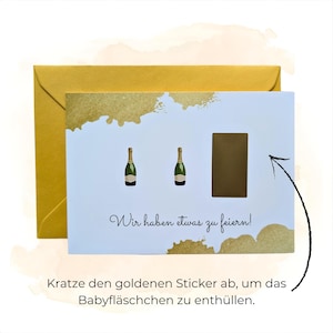 May include: A greeting card with a gold envelope. The card has two champagne bottle illustrations and the text "Wir haben etwas zu feiern!" with a scratch-off area. The text below says "Kratze den goldenen Sticker ab, um das Babyfl&auml;schchen zu enth&uuml;llen."