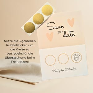 May include: A light peach-colored "Save the Date" card with two peach hearts and the text "Save the date" in black script. Three gold scratch-off stickers are included. The card has three circles and a baby onesie graphic.