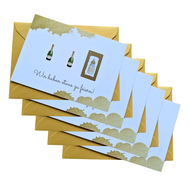May include: A stack of greeting cards with gold envelopes. The cards have a light blue background with gold accents and illustrations of champagne bottles and a baby bottle. The text on the card reads "Wir haben etwas zu feiern!"