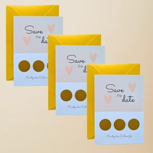 May include: A collection of wedding announcement cards with yellow envelopes. Each card has the text "Save the date" with a heart graphic. The bottom section of each card has gold scratch-off circles.