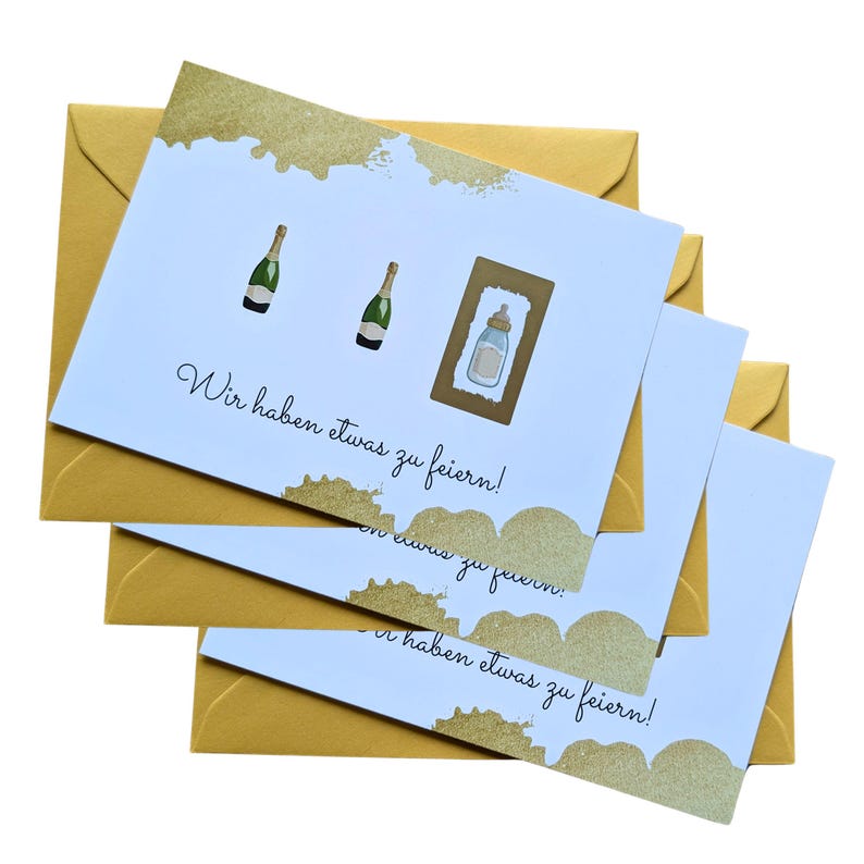 May include: A stack of greeting cards with gold envelopes. The cards have a light blue background with gold accents and the text "Wir haben etwas zu feiern!" Two champagne bottles and a baby bottle are illustrated on the cards.