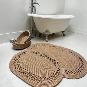 Pode incluir: Dois tapetes ovais de juta tecida com uma borda trançada decorativa e dois cestos de armazenamento ovais a condizer. Os tapetes apresentam um design central em espiral com uma borda em laço, enquanto os cestos são profundos e robustos.