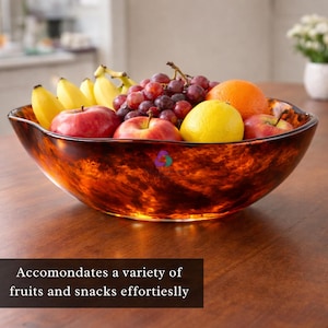 Puede incluir: Un frutero decorativo de vidrio color ámbar lleno de fruta fresca, incluyendo manzanas rojas, uvas, plátanos, una naranja y un limón. El cuenco está sobre una superficie de madera. El texto en la parte inferior dice: Accommodates a variety of fruits and snacks effortlessly.