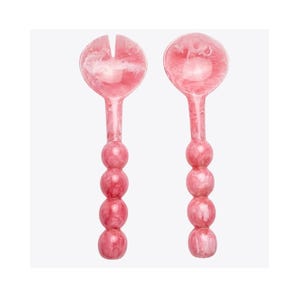 May include: Two pink salad servers with a marbled effect. One server has a slotted head, the other a round head. The handles are adorned with four stacked, round beads. The servers are made of a translucent material.