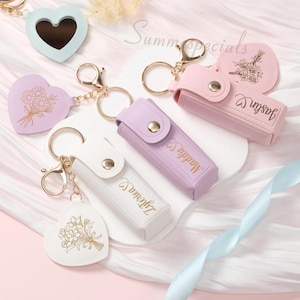 Può includere: Una collezione di portachiavi dai colori pastello, tra cui specchi a forma di cuore e custodie. Alcuni portachiavi presentano disegni floreali e nomi personalizzati. Hardware e chiusure color oro. Il testo "Summer Specials" è visibile sullo sfondo.