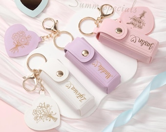 May include: A collection of keychains in pastel colors, including heart-shaped mirrors and cases. Some keychains feature floral designs and personalized names. Gold-colored hardware and clasps are used throughout the collection. The text "Summer Specials" is visible in the background.