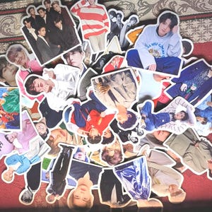 Puede incluir: Una colección de pegatinas troqueladas con varias imágenes de un grupo musical. Las pegatinas muestran a los miembros del grupo en diferentes poses y atuendos, con una variedad de colores y estilos. Las pegatinas están esparcidas sobre una superficie roja.