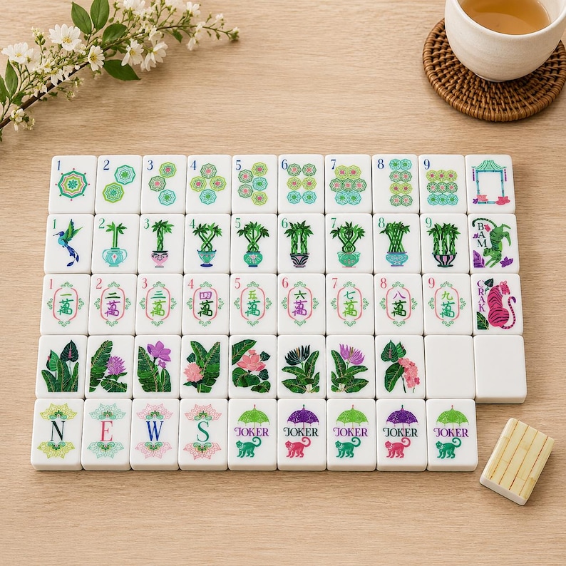 May include: A set of white rectangular mahjong tiles arranged in a grid, featuring colorful illustrations of plants, flowers, animals, and Chinese characters. The tiles include numbered suits, directional letters N, E, W, S, and Joker tiles with monkeys.