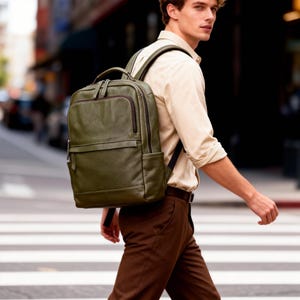 May include: Olive green leather backpack with multiple compartments and a top handle. The backpack has a rectangular shape with a front pocket and a zipper closure. The straps are black. The person is walking on a crosswalk.