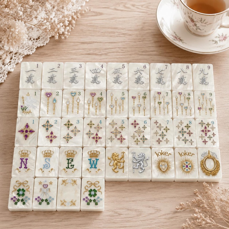 May include: A set of white pearlescent mahjong tiles arranged in a grid. The tiles feature engraved numbers one through nine, colorful gemstone-style star and wand motifs, letters N, S, E, W, lion figures, joker text, and floral clover designs.