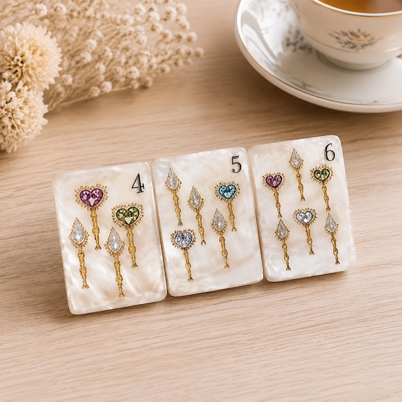 May include: Three rectangular white pearlescent display cards labeled 4, 5, and 6, each featuring gold-toned metal pins with heart and teardrop-shaped colorful gemstones. The pins are arranged in small clusters on each card, showcasing various jewel tones.
