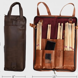 Op de afbeelding: Een bruine leren drumstoktas, 51 cm hoog en 20 cm breed als hij gesloten is, opent om drumstokken en vakken te onthullen. De open tas is 41 cm breed. Inclusief een vak voor een smartphone en een kleine spiegel.