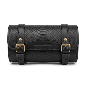 May include: A black cylindrical bag with a snakeskin texture, featuring two vertical straps with brass-toned metal buckles and studs. The front flap is embossed with the text FIRST STAR LEATHER in a centered, horizontal position.