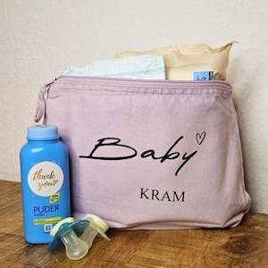 Könnte beinhalten: Eine hellviolette Babytasche mit dem Wort "Baby" und einem Herzdesign. Die Tasche enthält Windeln und Feuchttücher. Eine blaue Flasche Babypuder und zwei Schnuller befinden sich vor der Tasche.