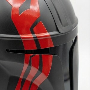Hand-painted steel Mandalorian helmet in black with a bold red Mythosaur logo; cosplay armor style for fans.