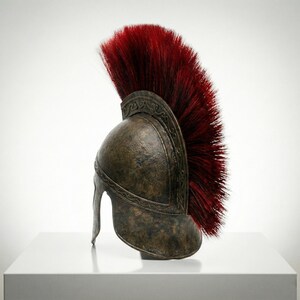 May include: A bronze-colored helmet with a weathered, textured finish and a prominent, tall crest made of stiff, deep red bristles. The helmet features an embossed, swirling decorative pattern along the ridge and a curved, protective face guard.