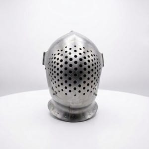 May include: A silver-colored medieval helmet with a rounded top and a faceplate covered in small, evenly spaced holes. The helmet sits on a white surface, showcasing its metallic sheen and historical design.