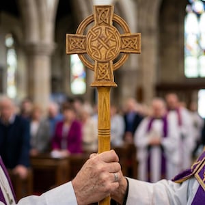 May include: A wooden processional cross featuring an intricate Celtic knotwork design carved into the circular head and arms. The cross is mounted on a long, smooth, cylindrical wooden staff, showcasing a natural light brown wood grain finish.