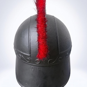 May include: A matte black helmet featuring a prominent, upright red crest made of stiff, fibrous material. The helmet has a smooth, rounded dome with a raised horizontal band across the front, decorated with a subtle, embossed wave-like pattern.