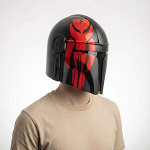 Hand-painted steel Mandalorian helmet in black with a bold red Mythosaur logo; cosplay armor style for fans.