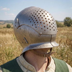 May include: A silver metal helmet with numerous small holes across the top. The helmet has a visor and is secured with a chin strap. The person is wearing a green vest and a quilted undergarment.