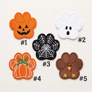 May include: Five embroidered paw-shaped patches labelled #1 through #5. Patch #1 is an orange jack-o'-lantern, #2 is a white ghost, #3 is a black spiderweb, #4 is an orange pumpkin with a green stem, and #5 is a brown turkey with a red wattle.