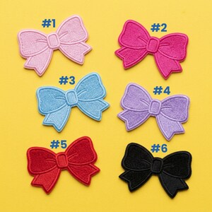 May include: Six embroidered bow patches in various colors: light pink, hot pink, light blue, lavender, red, and black. Each bow has a detailed stitched design and is numbered from one to six.