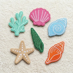 May include: Embroidered patches featuring sea life: a starfish, a seashell, a spiral shell, a conch shell, and coral. The patches are in shades of pink, blue, green, orange, and tan, with white stitching.