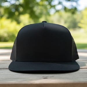 May include: A black trucker cap with a flat peak. The cap has a solid black front panel and a black mesh back. It is placed on a wooden surface with a blurred green background.