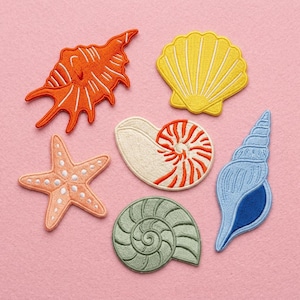 May include: A collection of embroidered patches featuring various sea shells and a starfish. The patches are in shades of orange, yellow, pink, blue, and green, with white and orange detailing. The patches are on a pink background.