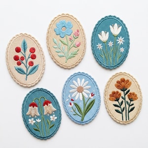 May include: A selection of seven embroidered floral patches in oval shapes. Each patch showcases a different flower design, such as berries, daisies, and tulips, in various colours. The patches have a scalloped edge and are set against a white background.