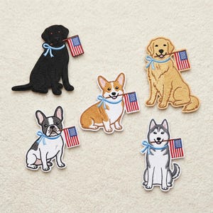 May include: Embroidered patches featuring various dog breeds, each holding a small American flag in their mouth. The dogs include a black Labrador, a golden retriever, a Corgi, a French Bulldog, and a Husky. Each dog has a blue ribbon.