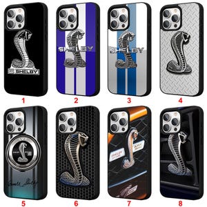 May include: A collection of phone cases featuring the Shelby Cobra logo. Designs include a black case with a white cobra, cases with blue and white stripes, and cases with a textured metal cobra.
