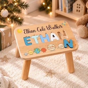 May include: A light-colored wooden puzzle stool featuring the name Ethan Cole Walker printed at the top. The name ETHAN is displayed in large, colorful, removable block letters, accompanied by a row of illustrated cartoon planets and a rocket.