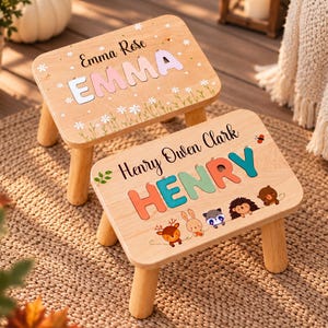 May include: Two light-colored wooden step stools with four legs. One stool features the name Emma Rose and the name EMMA in pastel letters with daisy illustrations. The other stool features the name Henry Owen Clark and the name HENRY in colorful letters with illustrations of a deer, rabbit, raccoon, hedgehog, and bear.