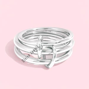 May include: A silver-colored ring with a multi-band design. The ring features several stacked bands with two vertical connecting elements. The text "Divine Jewels" is visible on the ring.