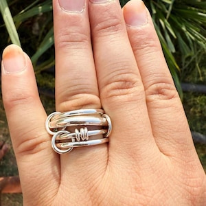 Peut inclure: Une bague en argent au design unique. La bague présente plusieurs bandes et éléments imbriqués, créant un aspect superposé et texturé. La bague est portée sur une main, mettant en valeur ses détails complexes et sa finition polie.