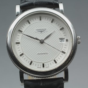 May include: A silver-toned Longines automatic watch with a white textured face, black hands, and a date display. The watch has a black leather band and is labeled "SWISS MADE".