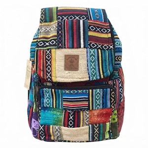May include: A backpack featuring a patchwork design of woven fabric in vibrant colors including blue, red, yellow, and green. The bag has a front pocket with a zipper, a top flap with a brown square patch displaying a leaf icon and the text HIMALAYAN, and a small paper tag attached to the side.