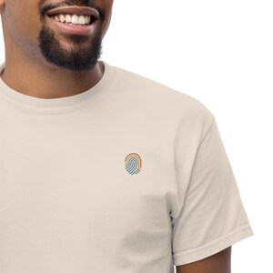 Peut inclure: T-shirt crème avec un petit motif d'empreinte digitale brodé aux couleurs de l'arc-en-ciel sur la poitrine gauche. Le t-shirt a un col rond classique et des manches courtes, fabriqué dans une matière douce et confortable.