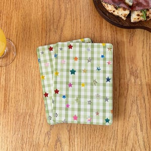 May include: Two rectangular coasters featuring a light green and white gingham check pattern. The surface of each coaster is decorated with a scattered print of small, multi-colored stars in shades of red, blue, yellow, pink, and silver.
