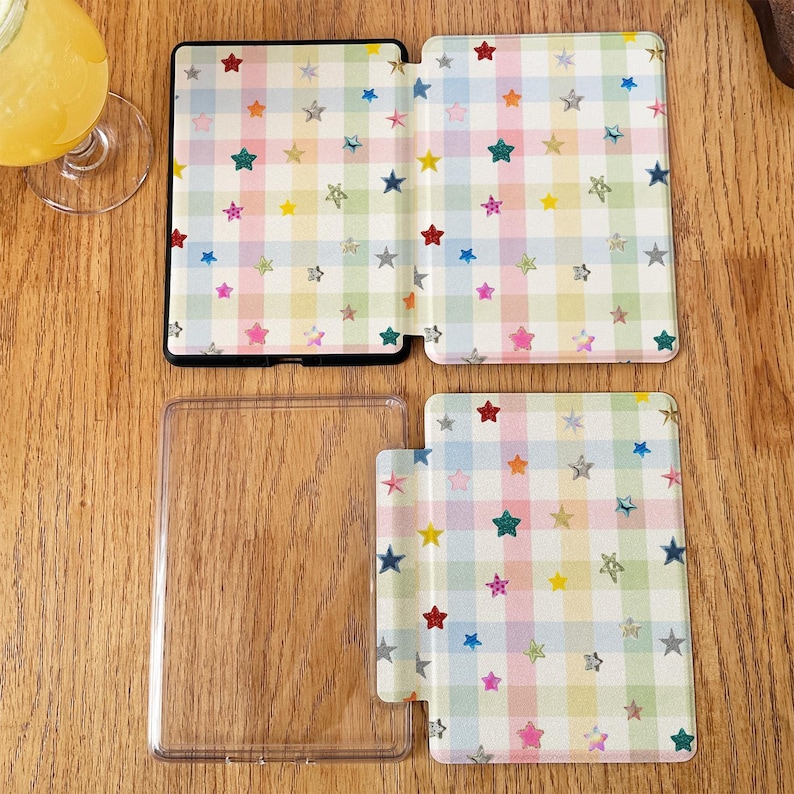 May include: Two rectangular e-reader cases featuring a pastel plaid pattern in shades of pink, blue, yellow, and green. The surface is decorated with small, multi-colored glittery stars scattered across the grid. One case is open, and one is flat.