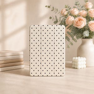 May include: A rectangular tablet case featuring a cream-coloured background with a repeating pattern of small black polka dots. The case has a tri-fold design with two vertical creases visible on the front surface, providing a structured appearance.