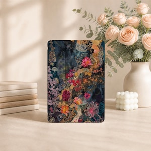 Puede incluir: Una funda rectangular para tableta con un fondo oscuro y evocador, adornado con un patrón floral vibrante e intrincado. El diseño incluye varias flores estilizadas en tonos rosa, naranja y dorado, sobre remolinos de color azul oscuro y negro.