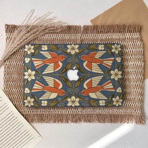 May include: A laptop hard shell case featuring a symmetrical pattern of four orange birds with cream-colored wings, surrounded by cream flowers and green leaves on a dark blue background, with a central cutout for the Apple logo.