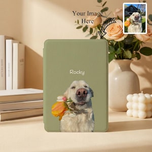 Peut inclure: Une housse de liseuse vert sauge avec un golden retriever souriant tenant une fleur. Le nom "Rocky" est imprimé au-dessus du chien. Une petite image du chien est dans le coin supérieur droit. Un vase de fleurs et une bougie sont en arrière-plan.
